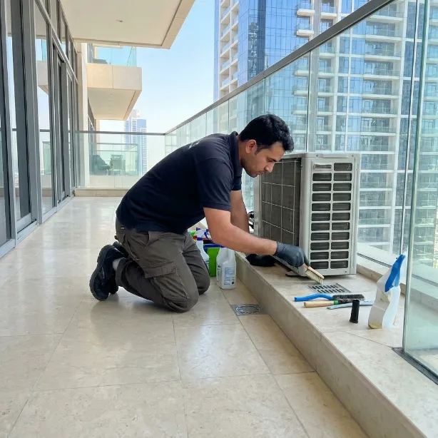 Professional cleaner servicing an outdoor AC unit on a Dubai apartment balcony